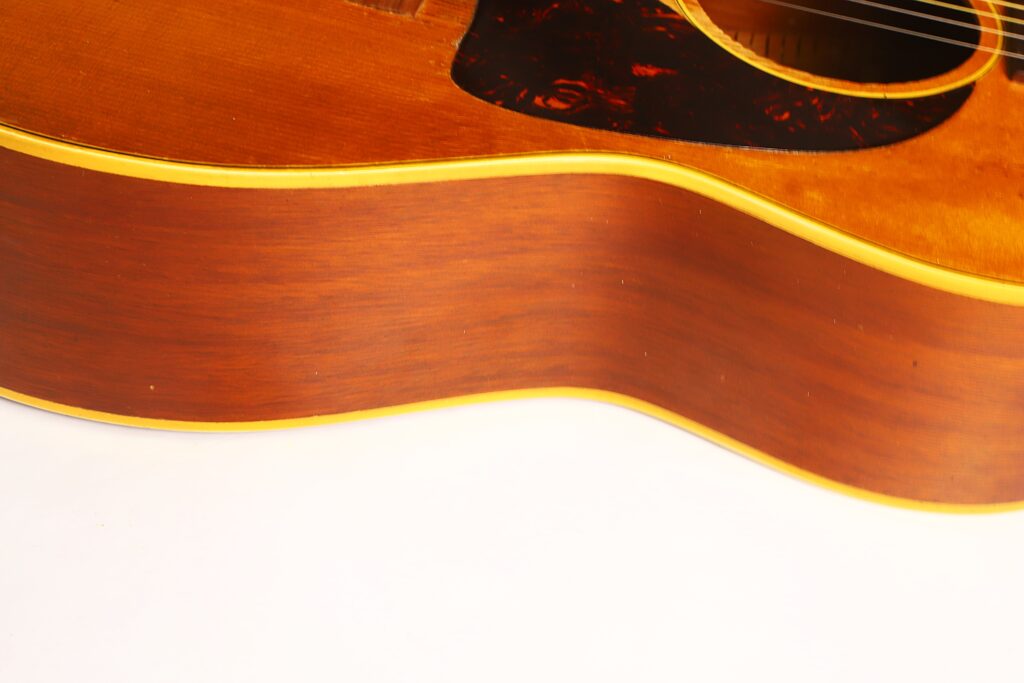 Nahaufnahme der Seite und des Korpus einer Gibson LG-3 Akustikgitarre aus dem Jahr 1954, die die Holzmaserung und einen Teil des Schalllochs vor weißem Hintergrund zeigt. Nahaufnahme der Seite und des Korpus einer Gibson LG-3 Akustikgitarre aus dem Jahr 1954, die die Holzmaserung und einen Teil des Schalllochs vor weißem Hintergrund zeigt.