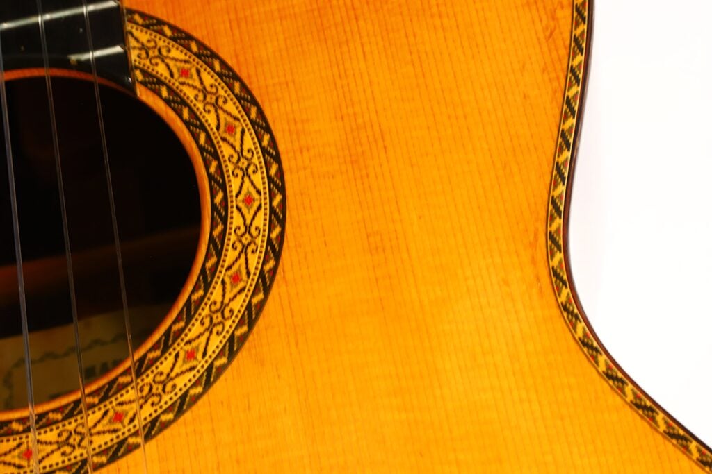 Nahaufnahme des Korpus der „Masaru Kohno Modell 50 1979 Klassische Gitarre“, die die aufwendigen Ziermuster rund um das Schallloch und den Rand hervorhebt; auf der linken Seite sind teilweise die Saiten zu sehen. Nahaufnahme des Korpus der „Masaru Kohno Modell 50 1979 Klassische Gitarre“, die die aufwendigen Ziermuster rund um das Schallloch und den Rand hervorhebt; auf der linken Seite sind teilweise die Saiten zu sehen.