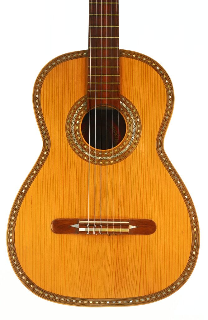 Eine Nahaufnahme der „Salvador Ibanez 1920 Klassische Gitarre“, die den Holzkorpus, das Schallloch mit dekorativer Einlage, die sechs Saiten und den unteren Teil des Griffbretts zeigt. Eine Nahaufnahme der „Salvador Ibanez 1920 Klassische Gitarre“, die den Holzkorpus, das Schallloch mit dekorativer Einlage, die sechs Saiten und den unteren Teil des Griffbretts zeigt.