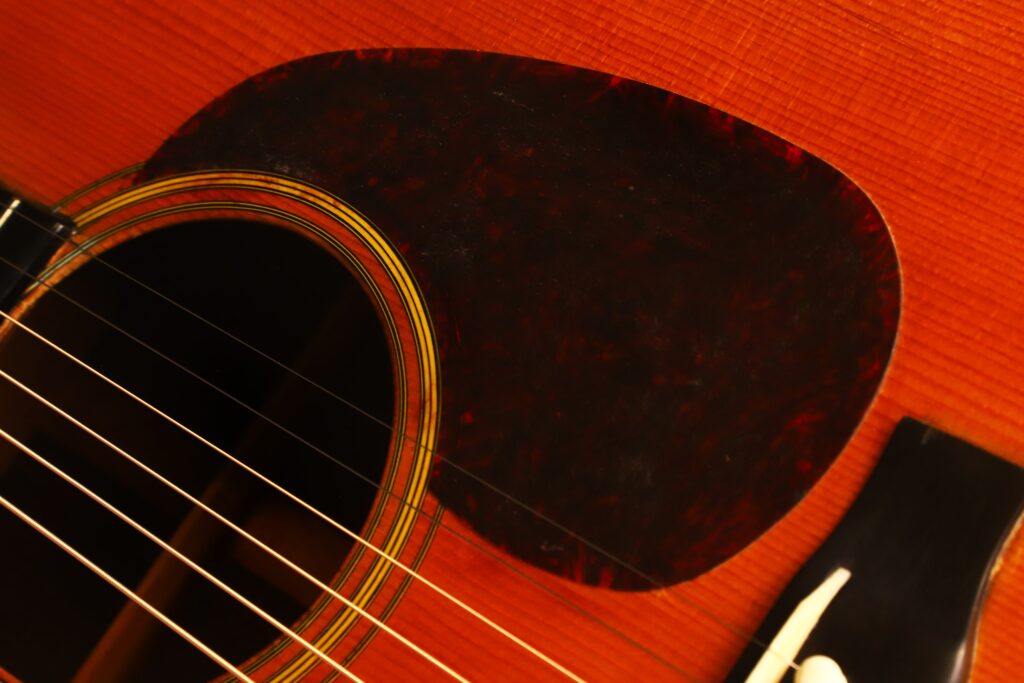 Nahaufnahme der Martin D-28 1941 Pre-War Akustikgitarre mit Fokus auf das Schallloch, die Saiten, das Pickguard mit Schildpatt-Muster und einen Teil des Stegs auf ihrem warmen Holzkorpus. Nahaufnahme der Martin D-28 1941 Pre-War Akustikgitarre mit Fokus auf das Schallloch, die Saiten, das Pickguard mit Schildpatt-Muster und einen Teil des Stegs auf ihrem warmen Holzkorpus.