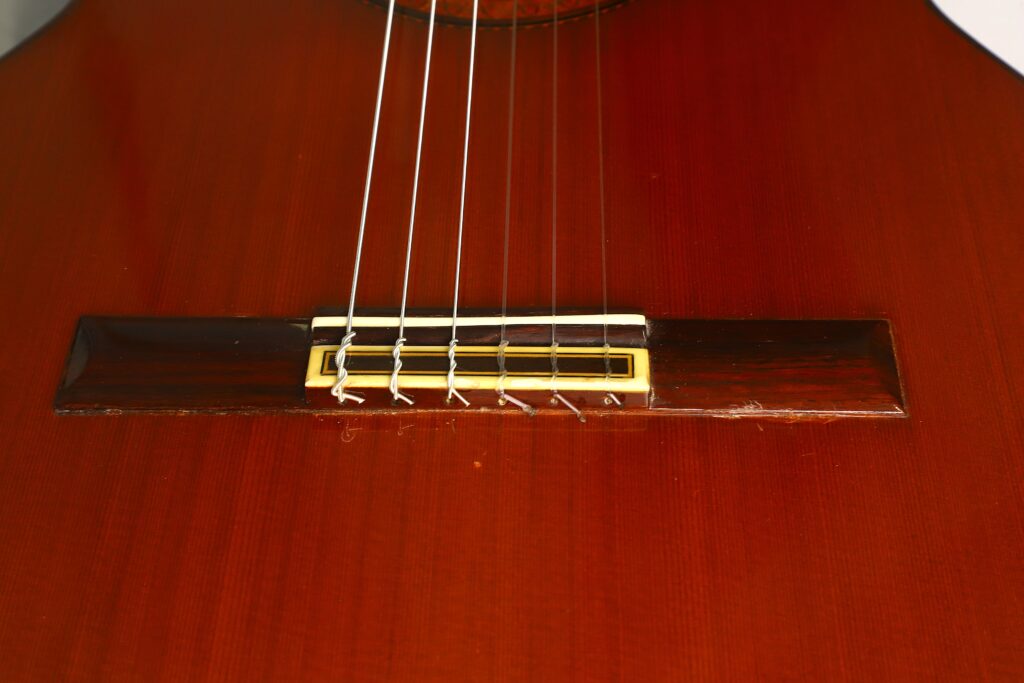 Nahaufnahme des Stegs und der Saiten einer Ramirez 1a 1985 Klassische Gitarre auf einem polierten Holzkorpus. Nahaufnahme des Stegs und der Saiten einer Ramirez 1a 1985 Klassische Gitarre auf einem polierten Holzkorpus.