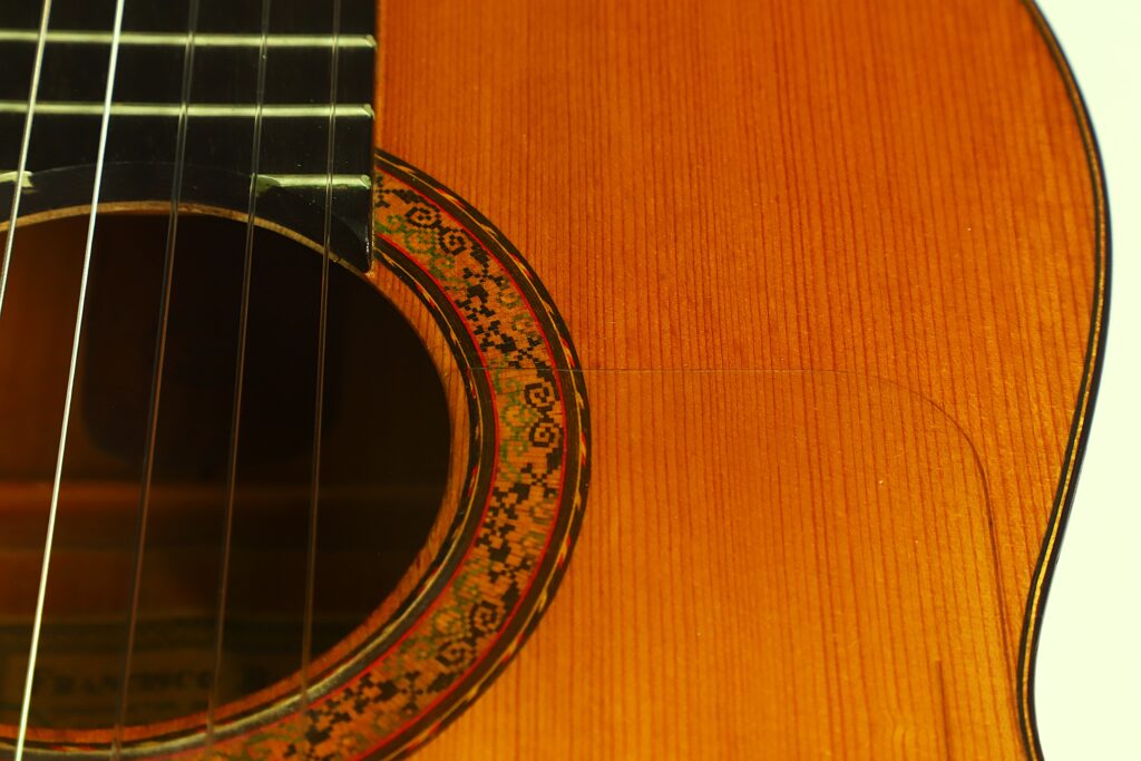 Nahaufnahme einer Flamenco-Gitarre von Francisco Barba aus dem Jahr 1966, die einen Teil des Schalllochs, die dekorative Rosette, die Saiten und die Holzmaserung zeigt. Nahaufnahme einer Flamenco-Gitarre von Francisco Barba aus dem Jahr 1966, die einen Teil des Schalllochs, die dekorative Rosette, die Saiten und die Holzmaserung zeigt.