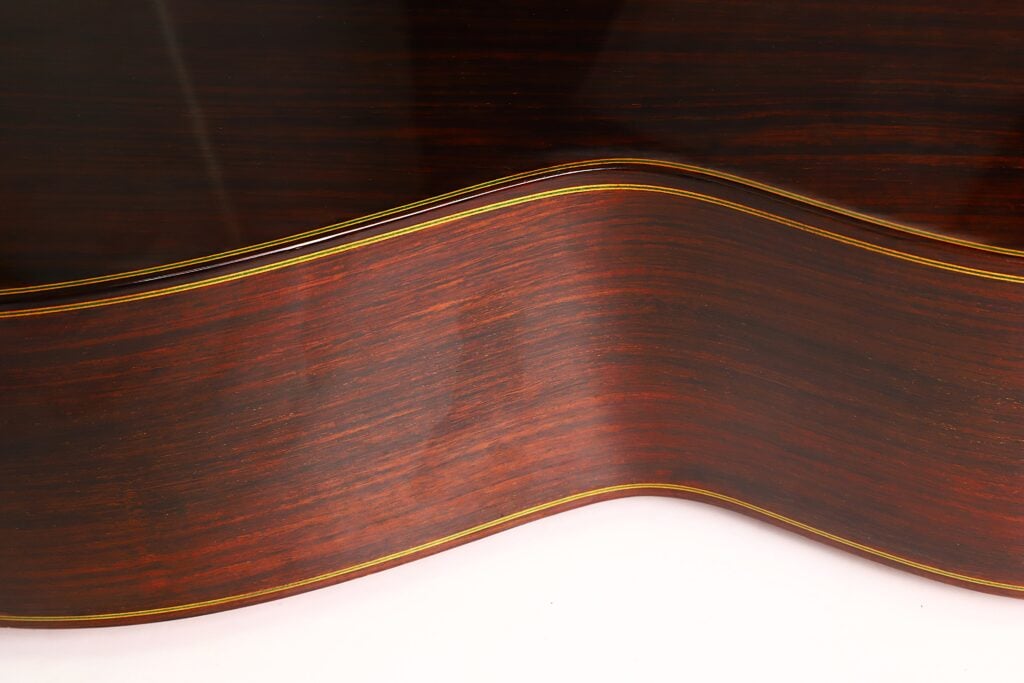 Nahaufnahme der Seiten- und Rückseite der Paulino Bernabe M-5 2008 Klassische Gitarre, die die natürliche Holzmaserung, die sanften Rundungen und eine schmale gelbe Zierlinie entlang der Kante hervorhebt. Nahaufnahme der Seiten- und Rückseite der Paulino Bernabe M-5 2008 Klassische Gitarre, die die natürliche Holzmaserung, die sanften Rundungen und eine schmale gelbe Zierlinie entlang der Kante hervorhebt.