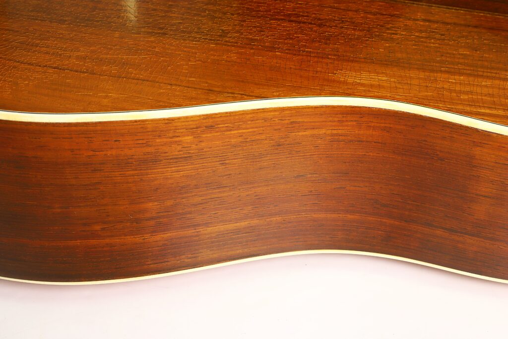 Nahaufnahme der Seite einer Martin D-28 1941 Pre-War Akustikgitarre, die die reichhaltige Holzmaserung, die anmutigen Rundungen und die cremefarbene Einfassung entlang der Kante hervorhebt. Nahaufnahme der Seite einer Martin D-28 1941 Pre-War Akustikgitarre, die die reichhaltige Holzmaserung, die anmutigen Rundungen und die cremefarbene Einfassung entlang der Kante hervorhebt.