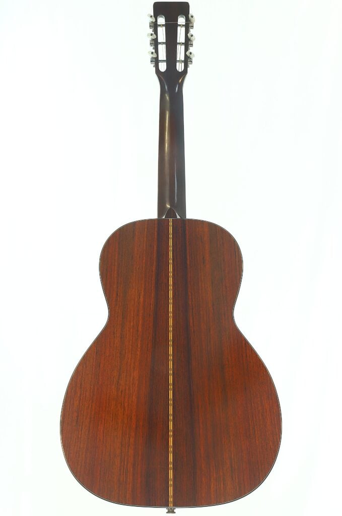 Die Rückansicht der Martin 00-21 Akustikgitarre aus dem Jahr 1986 besticht durch ihre dunkle Holzoberfläche, die durch eine vertikal in der Mitte verlaufende Zierintarsie hervorgehoben wird. Die Rückansicht der Martin 00-21 Akustikgitarre aus dem Jahr 1986 besticht durch ihre dunkle Holzoberfläche, die durch eine vertikal in der Mitte verlaufende Zierintarsie hervorgehoben wird.