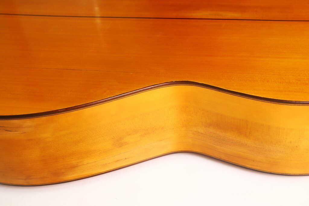 Nahaufnahme der Seite und Rückseite einer Flamenco-Gitarre von Francisco Barba aus dem Jahr 1966, die die reichhaltige Holzmaserung, die eleganten Rundungen und die glänzende Lackierung zur Geltung bringt. Nahaufnahme der Seite und Rückseite einer Flamenco-Gitarre von Francisco Barba aus dem Jahr 1966, die die reichhaltige Holzmaserung, die eleganten Rundungen und die glänzende Lackierung zur Geltung bringt.