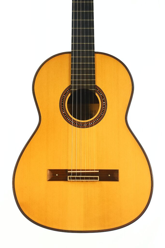 Die Matthias Hartig 2022 Hohlkehle Klassische Gitarre mit naturbelassener Holzoberfläche, sechs Saiten und einer dekorativen Schalllochrosette wird senkrecht vor einem schlichten weißen Hintergrund präsentiert. Die Matthias Hartig 2022 Hohlkehle Klassische Gitarre mit naturbelassener Holzoberfläche, sechs Saiten und einer dekorativen Schalllochrosette wird senkrecht vor einem schlichten weißen Hintergrund präsentiert.