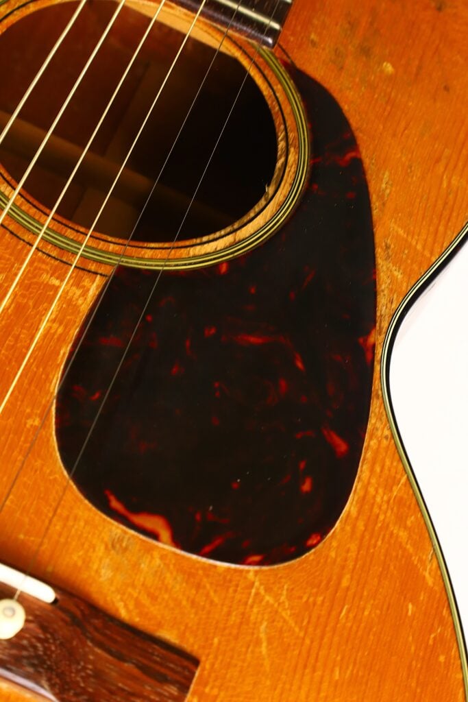 Nahaufnahme des Korpus der Martin 5-18 Akustikgitarre aus dem Jahr 1958, bei der das Schallloch, das Schlagbrett, die Saiten und die Maserung der Decke besonders hervorgehoben werden. Nahaufnahme des Korpus der Martin 5-18 Akustikgitarre aus dem Jahr 1958, bei der das Schallloch, das Schlagbrett, die Saiten und die Maserung der Decke besonders hervorgehoben werden.