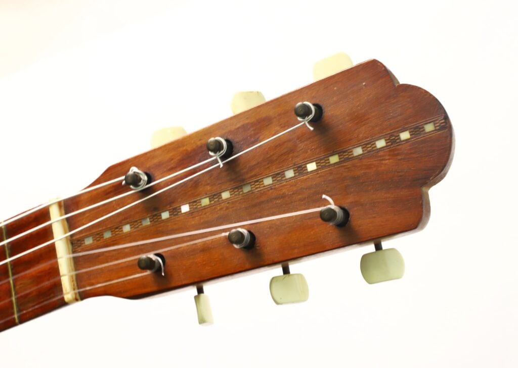 Nahaufnahme des Kopfes einer „Salvador Ibanez 1920 Klassische Gitarre“ mit sechs Stimmwirbeln mit weißen Knöpfen vor einem schlichten weißen Hintergrund. Nahaufnahme des Kopfes einer „Salvador Ibanez 1920 Klassische Gitarre“ mit sechs Stimmwirbeln mit weißen Knöpfen vor einem schlichten weißen Hintergrund.