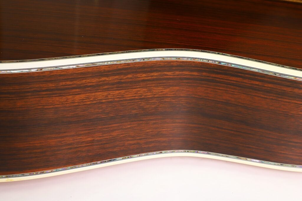 Nahaufnahme der Seite einer Martin D-45 Akustikgitarre aus dem Jahr 2009, die eine dunkle Holzmaserung mit glänzender Lackierung und einer cremefarbenen Einfassung entlang der Kante zeigt. Nahaufnahme der Seite einer Martin D-45 Akustikgitarre aus dem Jahr 2009, die eine dunkle Holzmaserung mit glänzender Lackierung und einer cremefarbenen Einfassung entlang der Kante zeigt.