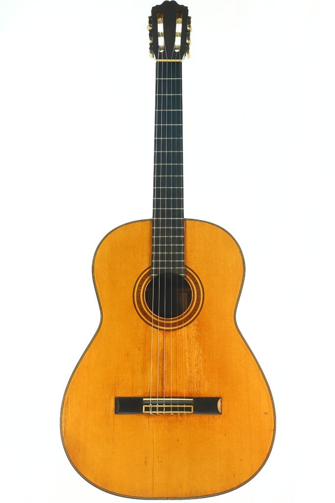 Die Angel Alonso 1936 Klassische Gitarre ist eine klassische Akustikgitarre mit naturbelassener Holzoberfläche, einem dunklen Griffbrett, sechs Saiten und einem aufwendigen Rosettenmuster, das das Schallloch umgibt und sich vor einem weißen Hintergrund abhebt. Die Angel Alonso 1936 Klassische Gitarre ist eine klassische Akustikgitarre mit naturbelassener Holzoberfläche, einem dunklen Griffbrett, sechs Saiten und einem aufwendigen Rosettenmuster, das das Schallloch umgibt und sich vor einem weißen Hintergrund abhebt.