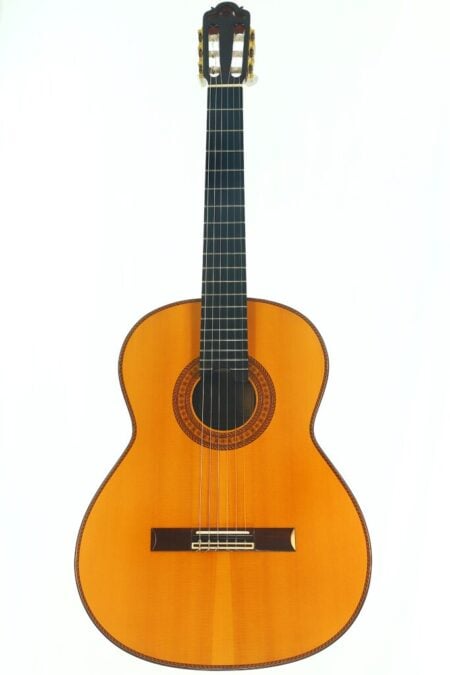 Die Hopf La Portentosa 2000 Klassiche Gitarre, eine klassische Akustikgitarre mit naturbelassenem Holzfinish, ist vor einem weißen Hintergrund abgebildet. Diese Gitarre verfügt über sechs Saiten, ein dunkles Griffbrett und dekorative Verzierungen rund um das Schallloch.