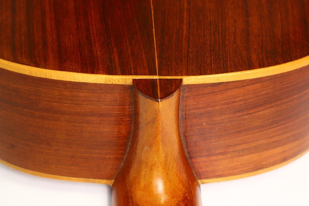 Nahaufnahme des Halsansatzes der „Salvador Ibanez 1920 Klassische Gitarre“, die poliertes braunes Holz mit sichtbarer Maserung und einen sanften, geschwungenen Übergang zwischen Korpus und Hals zeigt. Nahaufnahme des Halsansatzes der „Salvador Ibanez 1920 Klassische Gitarre“, die poliertes braunes Holz mit sichtbarer Maserung und einen sanften, geschwungenen Übergang zwischen Korpus und Hals zeigt.