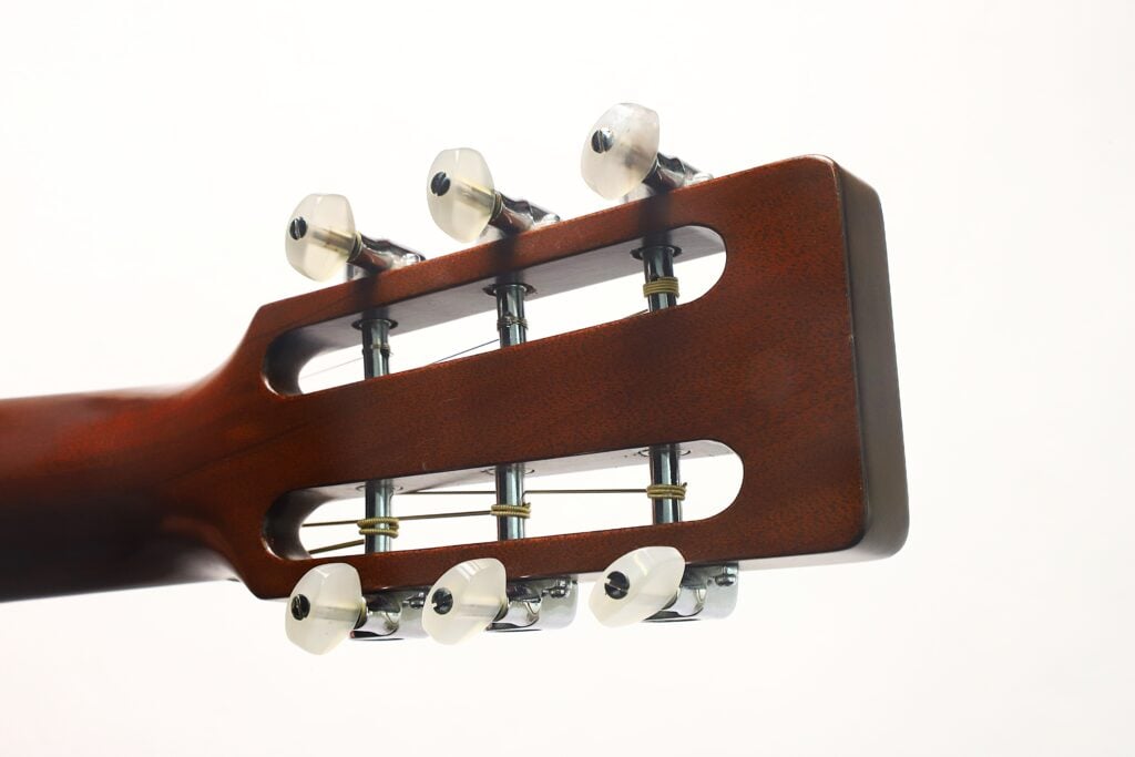 Nahaufnahme des Kopfes einer Martin 00-21 Akustikgitarre aus dem Jahr 1986, die sechs Stimmwirbel und Saiten mit Holzoptik vor einem weißen Hintergrund zeigt. Nahaufnahme des Kopfes einer Martin 00-21 Akustikgitarre aus dem Jahr 1986, die sechs Stimmwirbel und Saiten mit Holzoptik vor einem weißen Hintergrund zeigt.