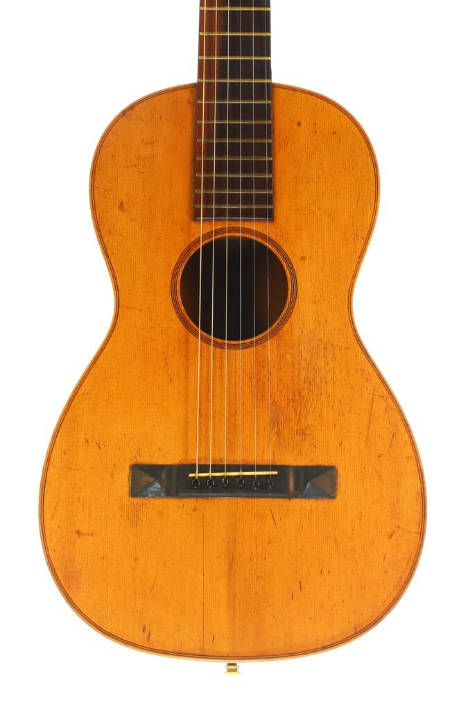 Eine Nahaufnahme der James Ashborn 1850 Parlor-Akustikgitarre, die den Holzkorpus, die sechs Saiten, das runde Schallloch, das dunkle Griffbrett und den rechteckigen Steg hervorhebt – alles vor einem weißen Hintergrund. Eine Nahaufnahme der James Ashborn 1850 Parlor-Akustikgitarre, die den Holzkorpus, die sechs Saiten, das runde Schallloch, das dunkle Griffbrett und den rechteckigen Steg hervorhebt – alles vor einem weißen Hintergrund.
