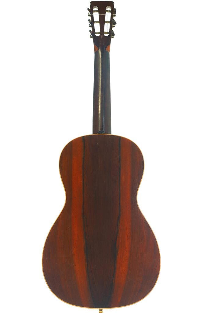 Die Rückseite der James Ashborn 1850 Parlor-Akustikgitarre ist mit einer glänzenden, dunklen Holzoberfläche mit markanten Maserungen versehen. Auch der Hals und die Kopfplatte sind zu sehen, an denen die Stimmwirbel zu erkennen sind. Die Rückseite der James Ashborn 1850 Parlor-Akustikgitarre ist mit einer glänzenden, dunklen Holzoberfläche mit markanten Maserungen versehen. Auch der Hals und die Kopfplatte sind zu sehen, an denen die Stimmwirbel zu erkennen sind.