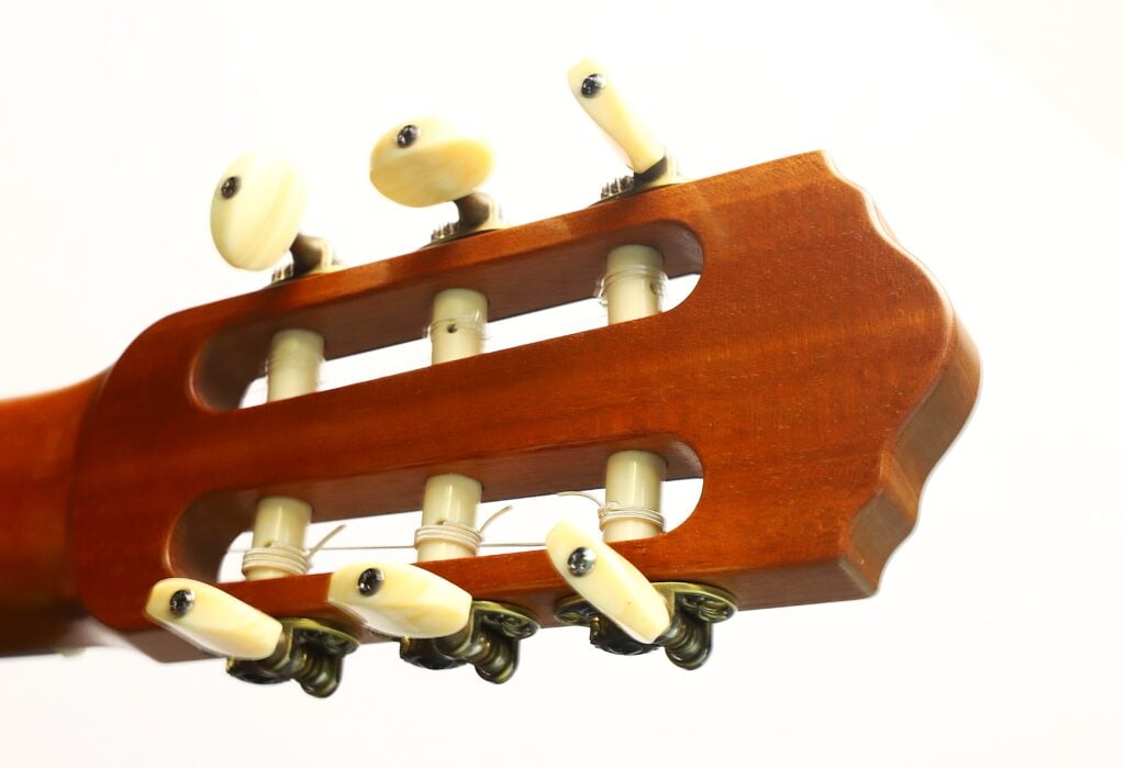 Nahaufnahme des Kopfes einer „Hohlkehle Klassische Gitarre“ von Matthias Hartig aus dem Jahr 2022 mit sechs weißen Stimmwirbeln vor weißem Hintergrund. Nahaufnahme des Kopfes einer „Hohlkehle Klassische Gitarre“ von Matthias Hartig aus dem Jahr 2022 mit sechs weißen Stimmwirbeln vor weißem Hintergrund.