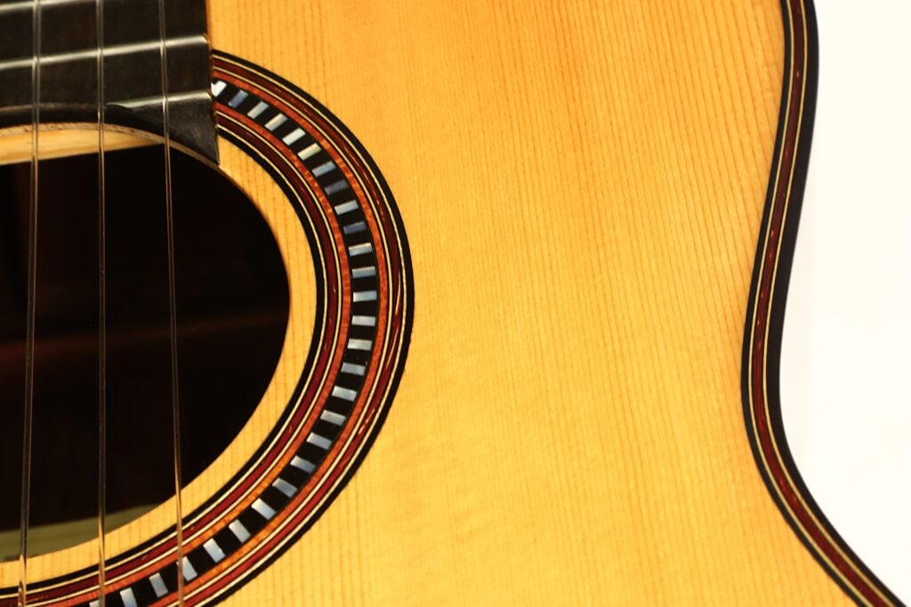 Nahaufnahme des Schalllochs, der Saiten und der dekorativen Rosette der „Matthias Hartig 2022 Hohlkehle Klassische Gitarre“, die die Holzmaserung und die detailreiche Handwerkskunst hervorhebt. Nahaufnahme des Schalllochs, der Saiten und der dekorativen Rosette der „Matthias Hartig 2022 Hohlkehle Klassische Gitarre“, die die Holzmaserung und die detailreiche Handwerkskunst hervorhebt.