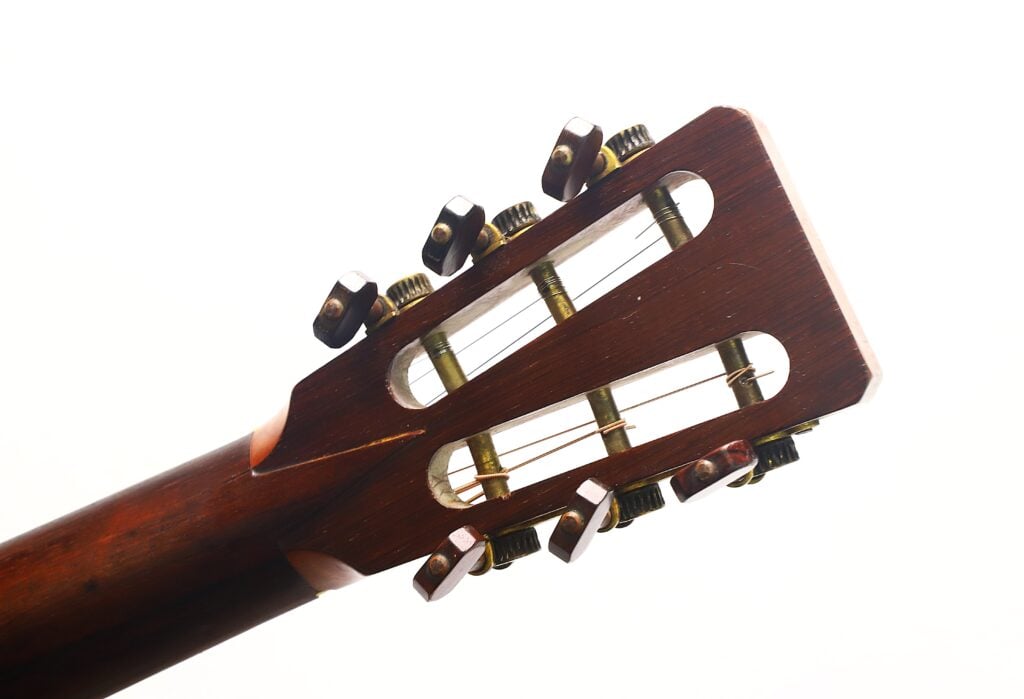Nahaufnahme des Kopfstücks der James Ashborn 1850 Parlor-Akustikgitarre mit sechs Stimmwirbeln – drei auf jeder Seite –, um die die Saiten gewickelt sind. Der Hintergrund ist weiß. Nahaufnahme des Kopfstücks der James Ashborn 1850 Parlor-Akustikgitarre mit sechs Stimmwirbeln – drei auf jeder Seite –, um die die Saiten gewickelt sind. Der Hintergrund ist weiß.
