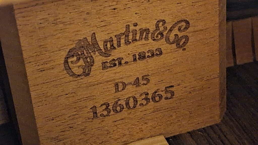 Ein graviertes Holzetikett mit der Aufschrift „Martin & Co. Est. 1833“, „D-45“ und die Seriennummer „1360365“ ist zu sehen, wobei die Holzmaserung deutlich erkennbar ist; das Etikett ist auf einer dunklen Holzoberfläche der Martin D-45 Akustikgitarre aus dem Jahr 2009 angebracht. Ein graviertes Holzetikett mit der Aufschrift „Martin & Co. Est. 1833“, „D-45“ und die Seriennummer „1360365“ ist zu sehen, wobei die Holzmaserung deutlich erkennbar ist; das Etikett ist auf einer dunklen Holzoberfläche der Martin D-45 Akustikgitarre aus dem Jahr 2009 angebracht.