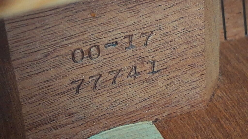Nahaufnahme einer Holzoberfläche mit eingeprägten Markierungen: „00-17“ über „77741“. Die Zahlen und Buchstaben sind in das Holz eingeprägt und geben wahrscheinlich die Modell- und Seriennummer einer Martin 00-17 Akustikgitarre aus dem Jahr 1941 an. Nahaufnahme einer Holzoberfläche mit eingeprägten Markierungen: „00-17“ über „77741“. Die Zahlen und Buchstaben sind in das Holz eingeprägt und geben wahrscheinlich die Modell- und Seriennummer einer Martin 00-17 Akustikgitarre aus dem Jahr 1941 an.
