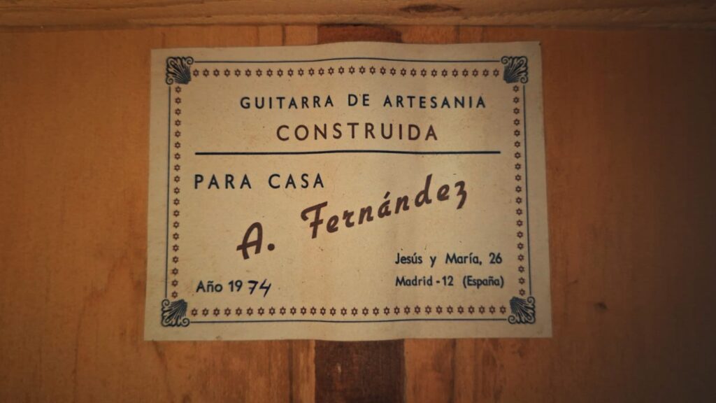 Auf einem alten Etikett im Inneren der Flamenco-Gitarre „Casa Arcangel Fernandez 1970“ steht: „Guitarra de Artesania construida para casa A. Fernández, Año 1974, Jesús y María, 26, Madrid – 12 (España)“, umrahmt von dekorativen Bordüren, die sich vom holzigen Innenraum abheben. Auf einem alten Etikett im Inneren der Flamenco-Gitarre „Casa Arcangel Fernandez 1970“ steht: „Guitarra de Artesania construida para casa A. Fernández, Año 1974, Jesús y María, 26, Madrid – 12 (España)“, umrahmt von dekorativen Bordüren, die sich vom holzigen Innenraum abheben.