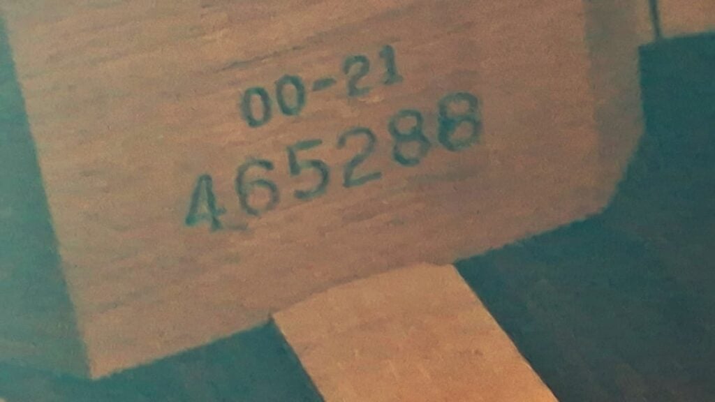 Eine Nahaufnahme der Holzoberfläche einer Martin 00-21 Akustikgitarre aus dem Jahr 1986, auf der die Zahlen 00-21 und 465288 in schwarzer Tinte eingeprägt sind. Eine Nahaufnahme der Holzoberfläche einer Martin 00-21 Akustikgitarre aus dem Jahr 1986, auf der die Zahlen 00-21 und 465288 in schwarzer Tinte eingeprägt sind.