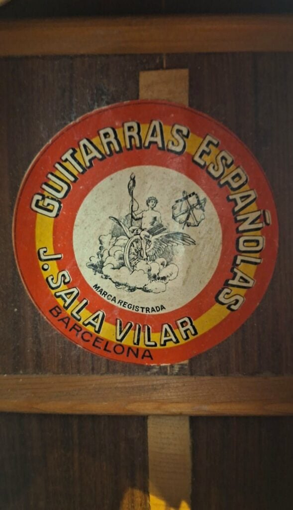 Auf dem runden Etikett im Inneren der „Salvador Ibanez 1920 Klassische Gitarre“ steht „GUITARRAS ESPAÑOLAS J. SALA VILAR BARCELONA“; in der Mitte ist eine geflügelte Figur abgebildet, die eine Fackel und einen Globus hält, umgeben von einem gelb-roten Rand. Auf dem runden Etikett im Inneren der „Salvador Ibanez 1920 Klassische Gitarre“ steht „GUITARRAS ESPAÑOLAS J. SALA VILAR BARCELONA“; in der Mitte ist eine geflügelte Figur abgebildet, die eine Fackel und einen Globus hält, umgeben von einem gelb-roten Rand.