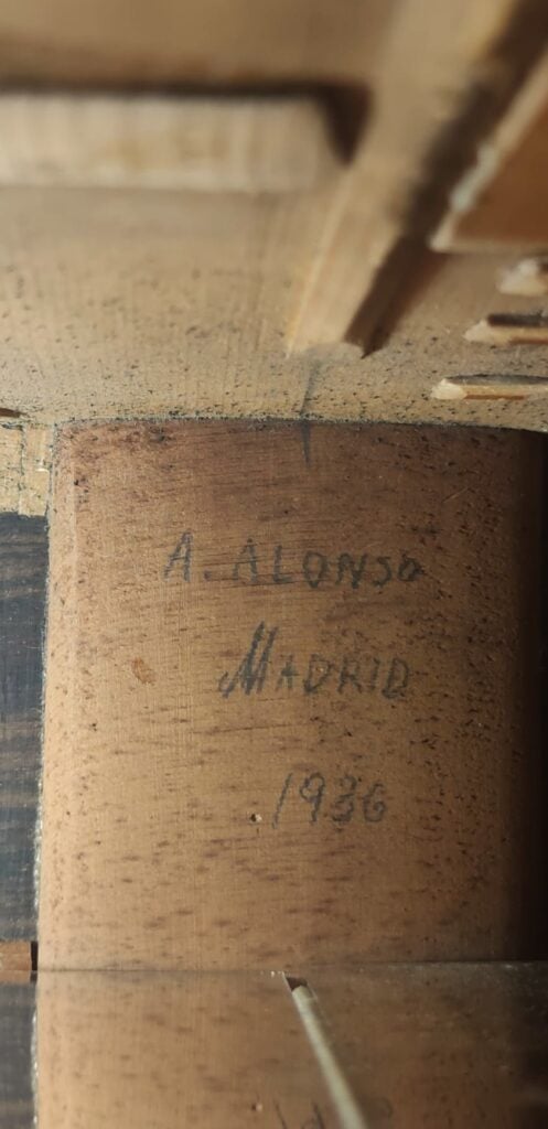 Nahaufnahme einer Holzoberfläche mit der handschriftlichen Aufschrift „A. Alonso Madrid 1936“, die möglicherweise auf den Hersteller und das Herstellungsjahr der „Angel Alonso 1936 Klassische Gitarre – Santos Hernandez“ hinweist. Nahaufnahme einer Holzoberfläche mit der handschriftlichen Aufschrift „A. Alonso Madrid 1936“, die möglicherweise auf den Hersteller und das Herstellungsjahr der „Angel Alonso 1936 Klassische Gitarre – Santos Hernandez“ hinweist.