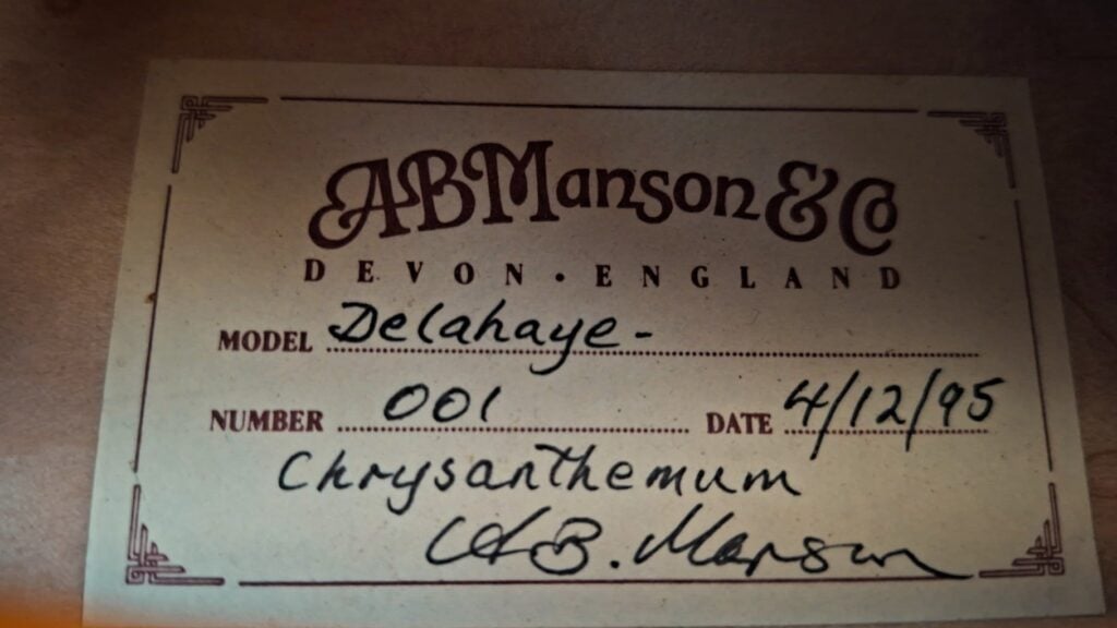 Ein historisches Etikett von AB Manson & Co. aus Devon, England, für die DeLaHaye 1995 Elektro-Akustik-Gitarre, Nummer 001, datiert auf den 12.04.95, mit einer Chrysantheme und einer handschriftlichen Unterschrift am unteren Rand. Ein historisches Etikett von AB Manson & Co. aus Devon, England, für die DeLaHaye 1995 Elektro-Akustik-Gitarre, Nummer 001, datiert auf den 12.04.95, mit einer Chrysantheme und einer handschriftlichen Unterschrift am unteren Rand.