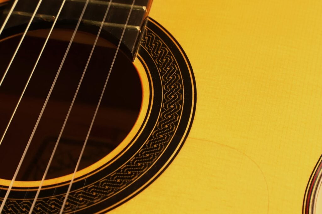 Nahaufnahme des hellen Korpus einer Antonio Aparicio Master Flamenco-Gitarre, auf der die Saiten, das runde Schallloch und das dekorative Rosettenmuster zu sehen sind. Nahaufnahme des hellen Korpus einer Antonio Aparicio Master Flamenco-Gitarre, auf der die Saiten, das runde Schallloch und das dekorative Rosettenmuster zu sehen sind.