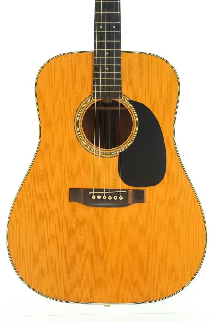 Eine Martin D-28 Akustikgitarre aus dem Jahr 1975 im sechssaitigen Akustik-Design mit einer Decke aus hellem Holz und einem schwarzen Schlagbrett. Eine Martin D-28 Akustikgitarre aus dem Jahr 1975 im sechssaitigen Akustik-Design mit einer Decke aus hellem Holz und einem schwarzen Schlagbrett.