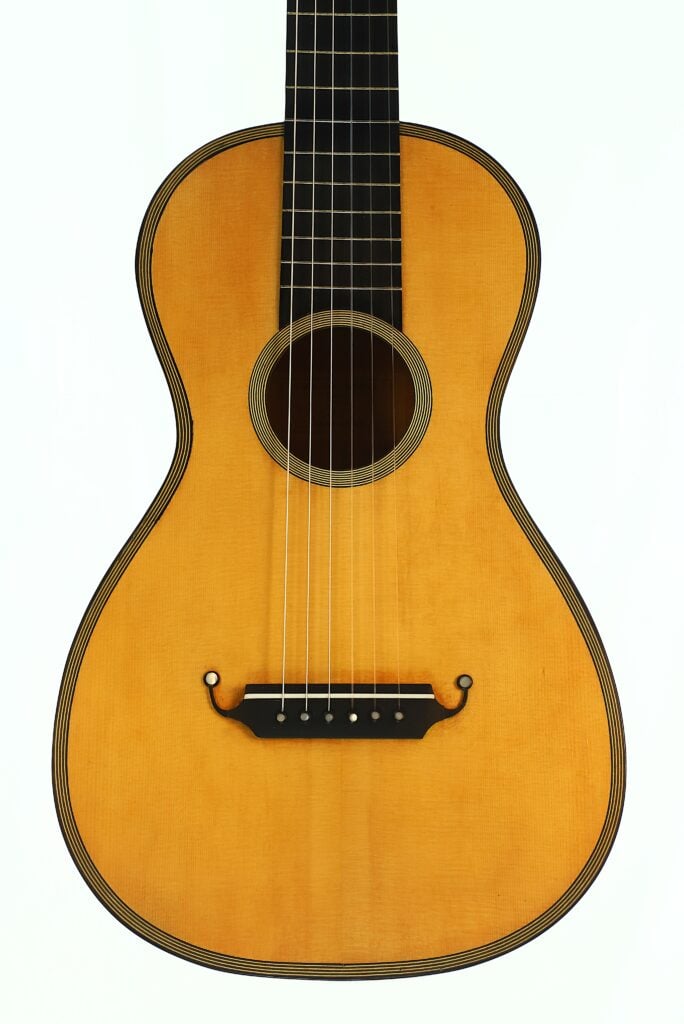 Nahaufnahme einer Romantikgitarre Modell Lacote von Carlos Gass Castañeda aus dem Jahr 1995 mit einer hellen Holzdecke, einem runden Schallloch und einem dekorativen schwarzen Steg. Nahaufnahme einer Romantikgitarre Modell Lacote von Carlos Gass Castañeda aus dem Jahr 1995 mit einer hellen Holzdecke, einem runden Schallloch und einem dekorativen schwarzen Steg.