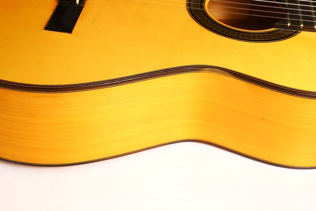 Nahaufnahme des hellen Korpus einer Antonio Aparicio Master Flamenco-Gitarre, auf der die Einbuchtung, das Schallloch und die Saiten zu sehen sind. Nahaufnahme des hellen Korpus einer Antonio Aparicio Master Flamenco-Gitarre, auf der die Einbuchtung, das Schallloch und die Saiten zu sehen sind.