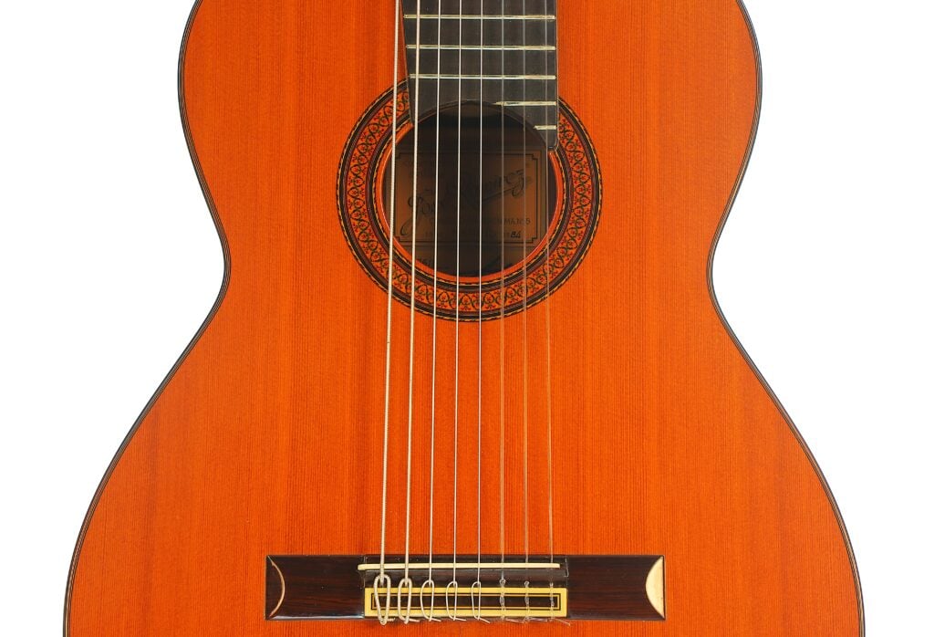 Nahaufnahme der Decke und des Stegs einer 8-saitigen klassischen Gitarre von José Ramírez aus dem Jahr 1984 mit einer kunstvoll verzierten runden Rosette. Nahaufnahme der Decke und des Stegs einer 8-saitigen klassischen Gitarre von José Ramírez aus dem Jahr 1984 mit einer kunstvoll verzierten runden Rosette.