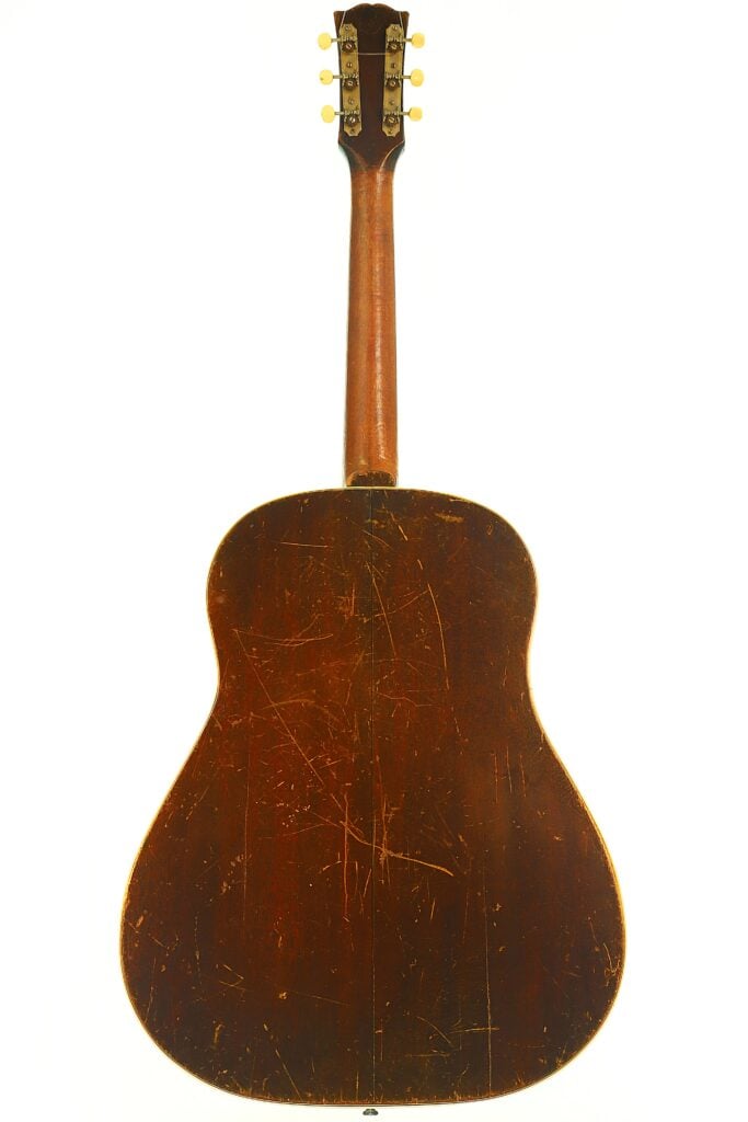 Rückansicht einer Gibson J-45 Banner Akustikgitarre aus dem Jahr 1943 mit einem abgenutzten, zerkratzten Korpus aus dunklem Holz und einem Holzhals mit sechs Stimmwirbeln. Rückansicht einer Gibson J-45 Banner Akustikgitarre aus dem Jahr 1943 mit einem abgenutzten, zerkratzten Korpus aus dunklem Holz und einem Holzhals mit sechs Stimmwirbeln.
