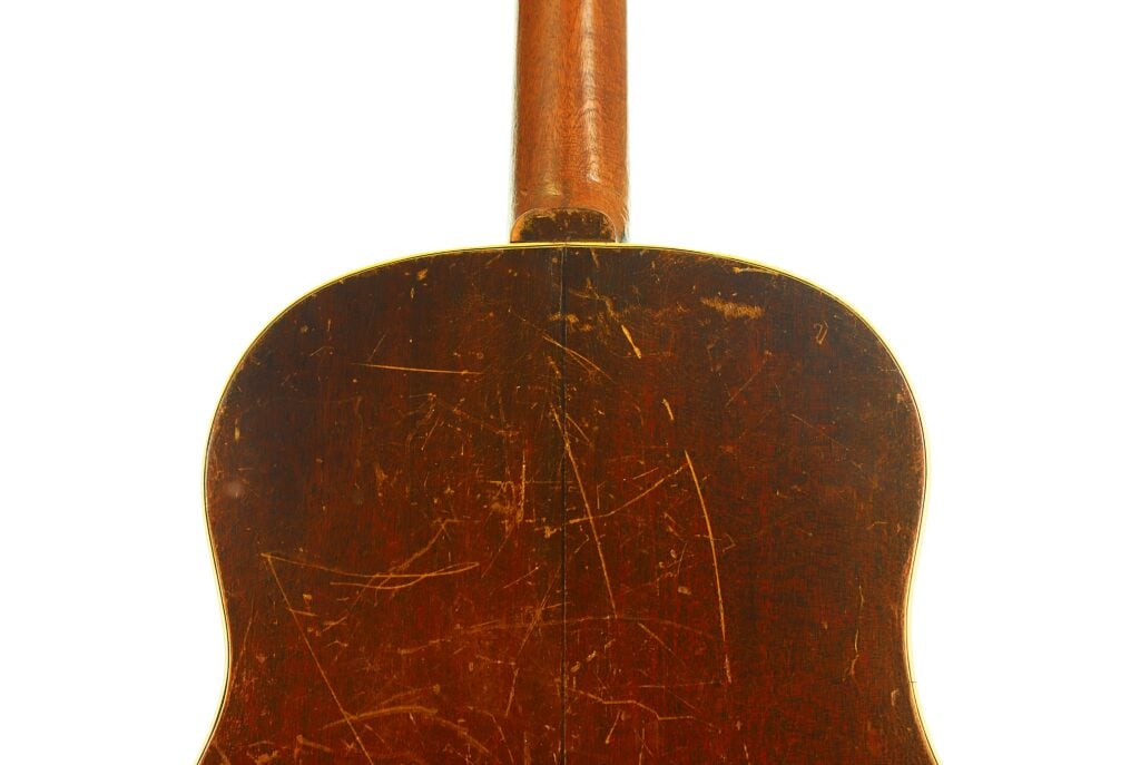 Rückansicht des Korpus einer abgenutzten Gibson J-45 Banner Akustikgitarre aus dem Jahr 1943 mit dunkler Holzoberfläche und starken Kratzern. Rückansicht des Korpus einer abgenutzten Gibson J-45 Banner Akustikgitarre aus dem Jahr 1943 mit dunkler Holzoberfläche und starken Kratzern.