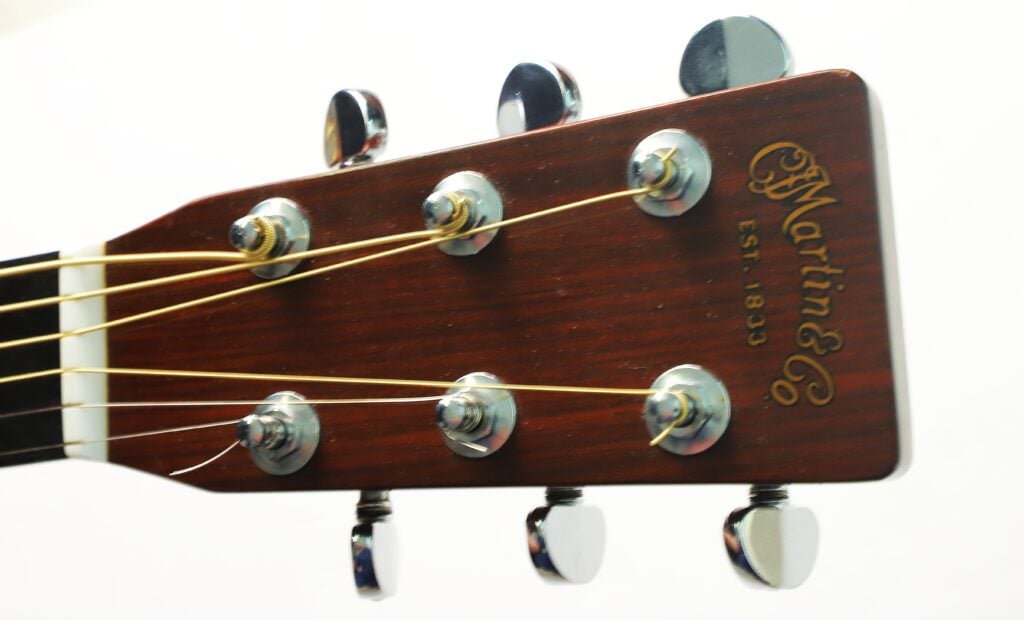 Kopfplatte einer Martin D-28 Akustikgitarre aus dem Jahr 1975 mit sechs Stimmwirbeln und aufgezogenen Saiten. Kopfplatte einer Martin D-28 Akustikgitarre aus dem Jahr 1975 mit sechs Stimmwirbeln und aufgezogenen Saiten.