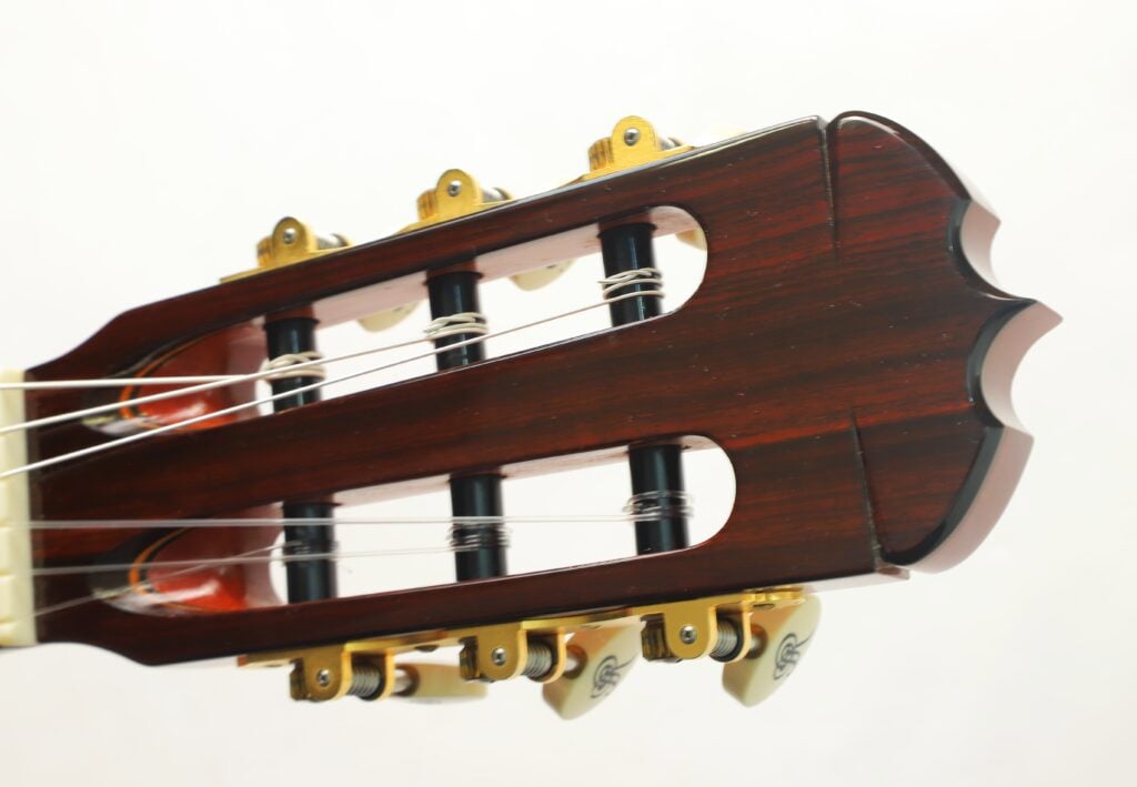 Kopfplatte der klassischen Gitarre Jose Ramirez 1a 2019 C-650 Tradicional mit dunklem Holzfurnier, goldenen Stimmmechaniken und weißen Knöpfen. Kopfplatte der klassischen Gitarre Jose Ramirez 1a 2019 C-650 Tradicional mit dunklem Holzfurnier, goldenen Stimmmechaniken und weißen Knöpfen.