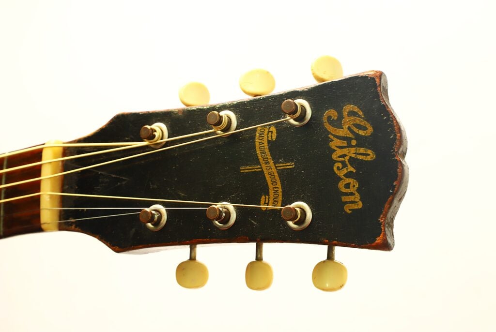 Kopfplatte einer Gibson J-45 Banner Akustikgitarre aus dem Jahr 1943 mit Stimmwirbeln und einem Banner-Logo mit der Aufschrift Only a Gibson is Good Enough. Kopfplatte einer Gibson J-45 Banner Akustikgitarre aus dem Jahr 1943 mit Stimmwirbeln und einem Banner-Logo mit der Aufschrift Only a Gibson is Good Enough.