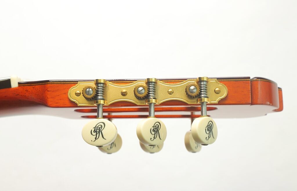 Seitenansicht des Kopfes einer Jose Ramirez 1a 2019 C-650 Tradicional Klassische Gitarre mit goldenen Stimmmechaniken, cremefarbenen Knöpfen und einem verzierten Logo. Seitenansicht des Kopfes einer Jose Ramirez 1a 2019 C-650 Tradicional Klassische Gitarre mit goldenen Stimmmechaniken, cremefarbenen Knöpfen und einem verzierten Logo.