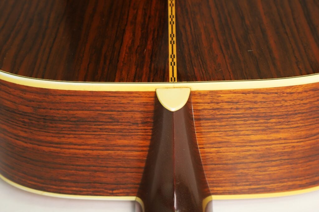 Nahaufnahme des Halsfußes und des Rückens einer Martin D-28 Akustikgitarre aus dem Jahr 1975, die die Holzmaserung und den dekorativen Mittelstreifen zeigt. Nahaufnahme des Halsfußes und des Rückens einer Martin D-28 Akustikgitarre aus dem Jahr 1975, die die Holzmaserung und den dekorativen Mittelstreifen zeigt.