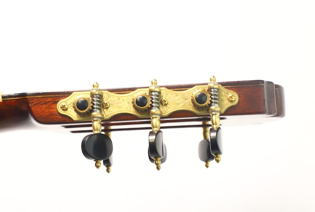 Seitenansicht einer Richard-Howell-Klassikgitarre aus dem Jahr 1980 mit gravierten goldenen Stimmmechaniken und schwarzen Stimmknöpfen. Seitenansicht einer Richard-Howell-Klassikgitarre aus dem Jahr 1980 mit gravierten goldenen Stimmmechaniken und schwarzen Stimmknöpfen.