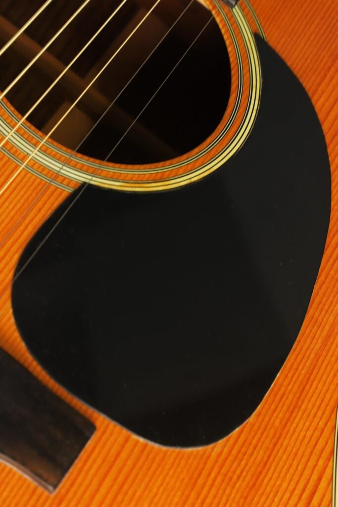 Nahaufnahme des Korpus der Martin D-28 Akustikgitarre aus dem Jahr 1975, mit Fokus auf das Schallloch, die Saiten und das schwarze Schlagbrett. Nahaufnahme des Korpus der Martin D-28 Akustikgitarre aus dem Jahr 1975, mit Fokus auf das Schallloch, die Saiten und das schwarze Schlagbrett.