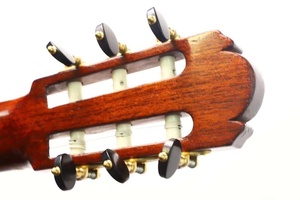 Kopfplatte einer Klassische Gitarre von Richard Howell aus dem Jahr 1980 mit Holzrahmen, weißen Saitenrollen und dunklen Stimmwirbeln. Kopfplatte einer Klassische Gitarre von Richard Howell aus dem Jahr 1980 mit Holzrahmen, weißen Saitenrollen und dunklen Stimmwirbeln.