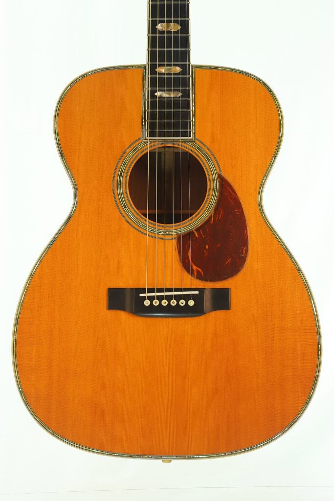 Martin SOM-45 Akustikgitarre aus dem Jahr 1977 mit einem orangefarbenen Korpus, einem dunklen Griffbrett mit Block-Einlagen und einem Schlagbrett mit Schildpatt-Muster. Martin SOM-45 Akustikgitarre aus dem Jahr 1977 mit einem orangefarbenen Korpus, einem dunklen Griffbrett mit Block-Einlagen und einem Schlagbrett mit Schildpatt-Muster.