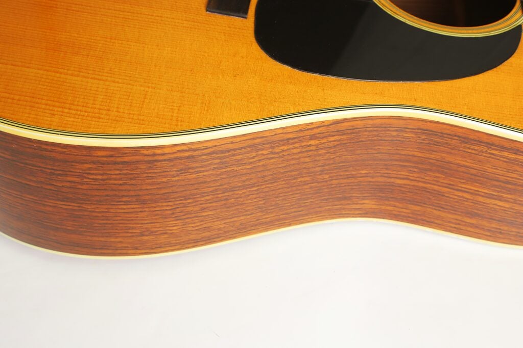 Nahaufnahme des Korpus einer Martin D-28 Akustikgitarre aus dem Jahr 1975, auf der die Holzmaserung, das Schlagbrett und das Schallloch zu sehen sind. Nahaufnahme des Korpus einer Martin D-28 Akustikgitarre aus dem Jahr 1975, auf der die Holzmaserung, das Schlagbrett und das Schallloch zu sehen sind.