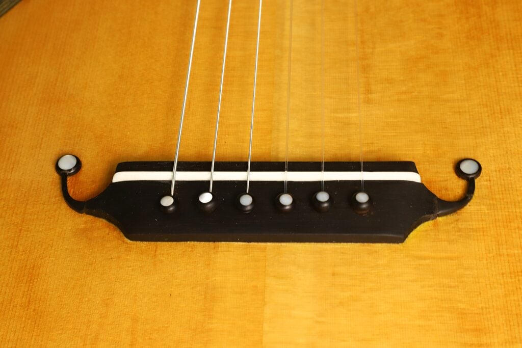 Nahaufnahme des Stegs einer Modell Lacote Romantikgitarre von Carlos Gass Castañeda aus dem Jahr 1995, mit sechs Saiten, die an mit Perlmutt eingelegten Stiften befestigt sind. Nahaufnahme des Stegs einer Modell Lacote Romantikgitarre von Carlos Gass Castañeda aus dem Jahr 1995, mit sechs Saiten, die an mit Perlmutt eingelegten Stiften befestigt sind.