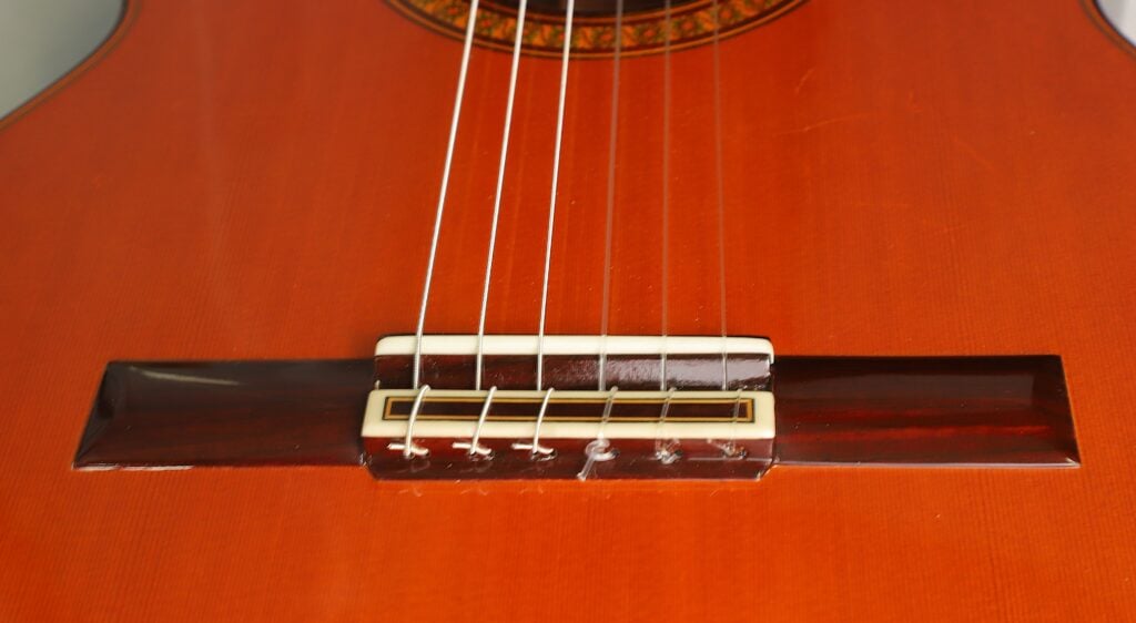 Nahaufnahme der Nylonsaiten und des Saitenhalters am Steg einer Jose Ramirez 1a 2019 C-650 Tradicional Klassische Gitarre. Nahaufnahme der Nylonsaiten und des Saitenhalters am Steg einer Jose Ramirez 1a 2019 C-650 Tradicional Klassische Gitarre.