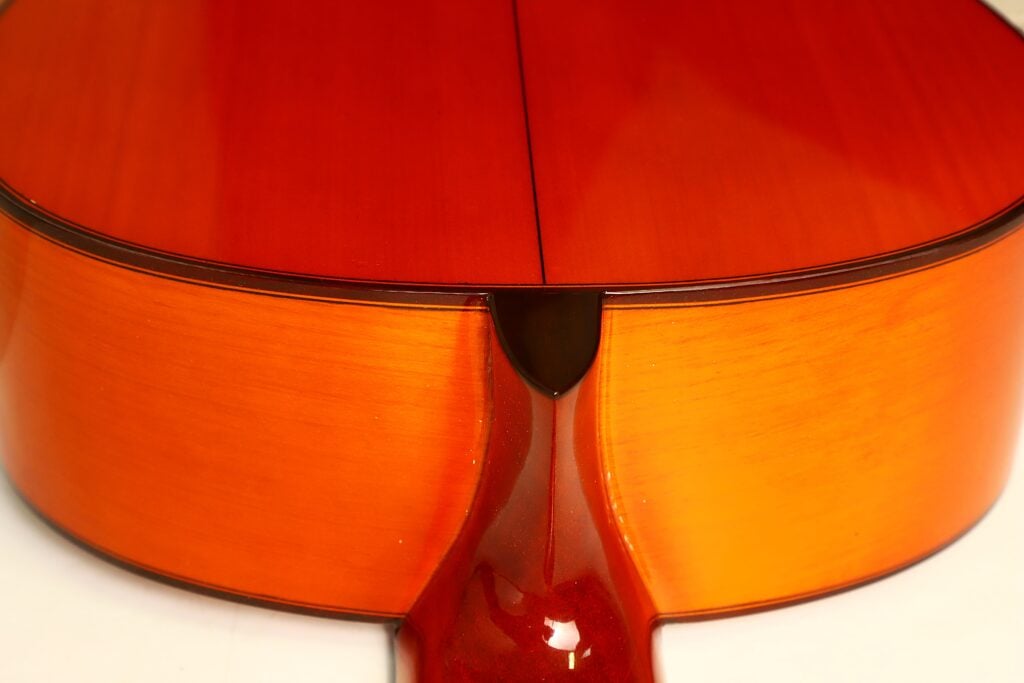 Nahaufnahme des Halsfußes, wo der Hals auf den Korpus einer orangefarbenen Flamenco-Gitarre von Conde Hermanos aus dem Jahr 1989 trifft. Nahaufnahme des Halsfußes, wo der Hals auf den Korpus einer orangefarbenen Flamenco-Gitarre von Conde Hermanos aus dem Jahr 1989 trifft.